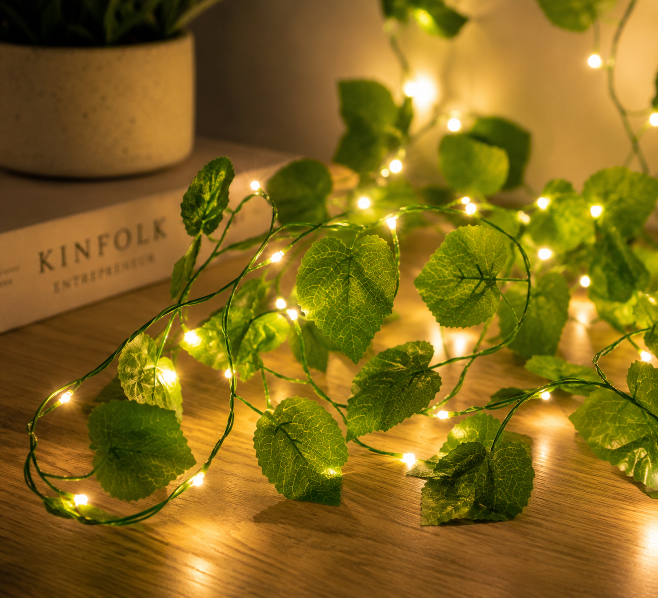 String lights with leaf design on a wooden surface next to a book titled 'KINFOLK'.